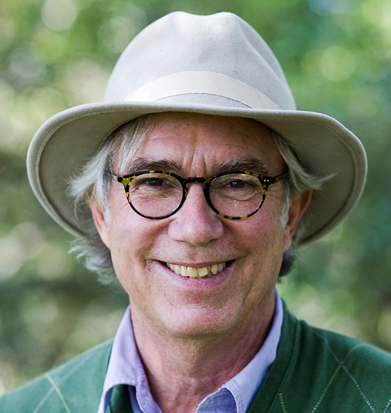 Smiling person wearing glasses and a hat with a blurred green background.