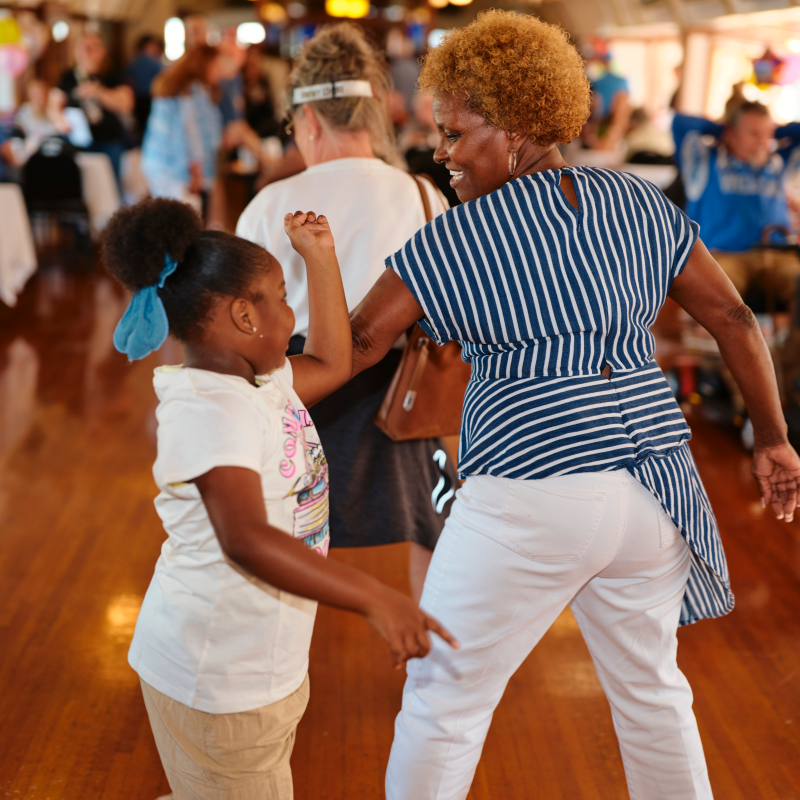Belle Birthday People dancing together in a room with wooden floors and tables in the background.