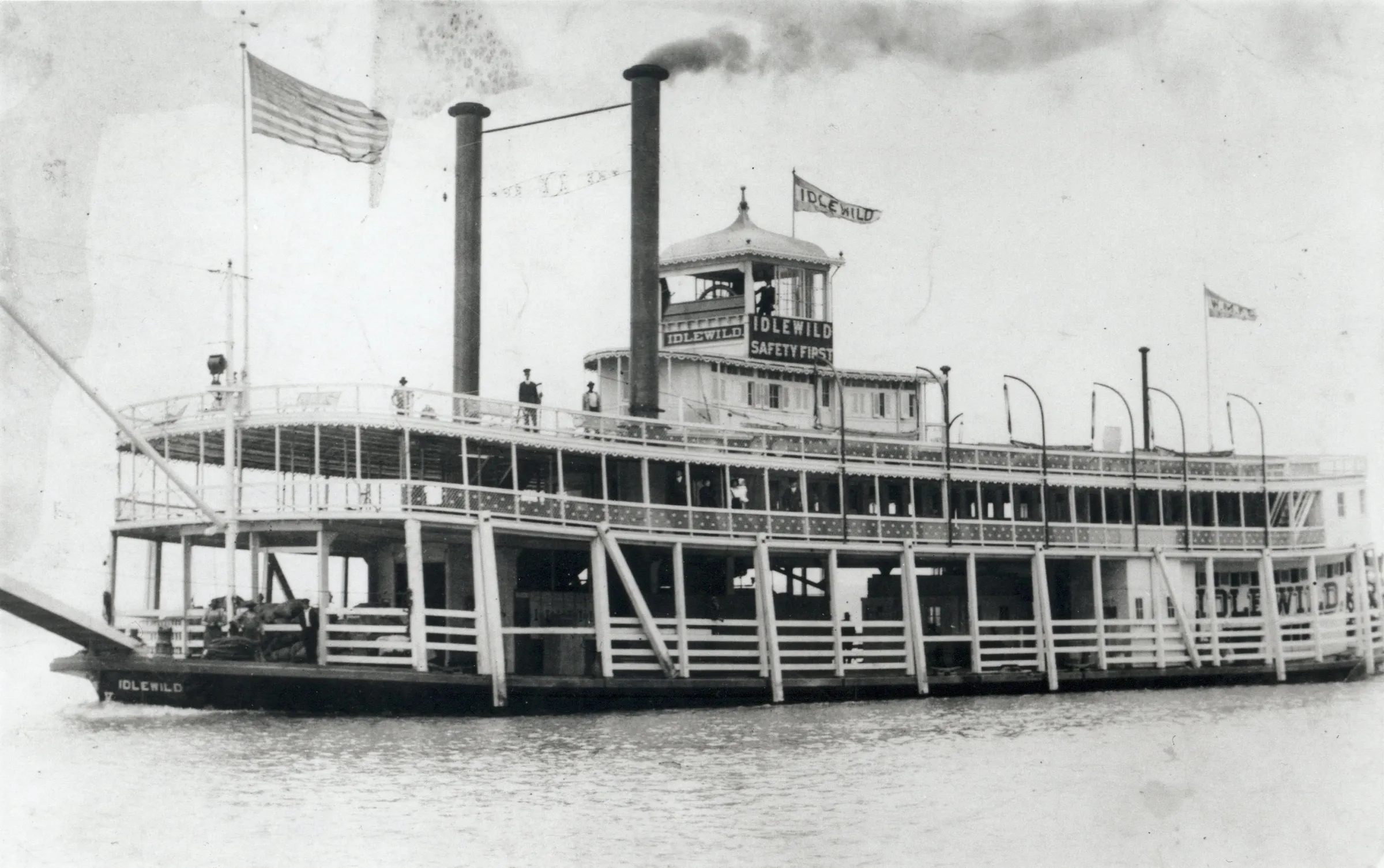 Idlewild Vintage steamboat Idlewild with flags on a river, two smokestacks emitting smoke.