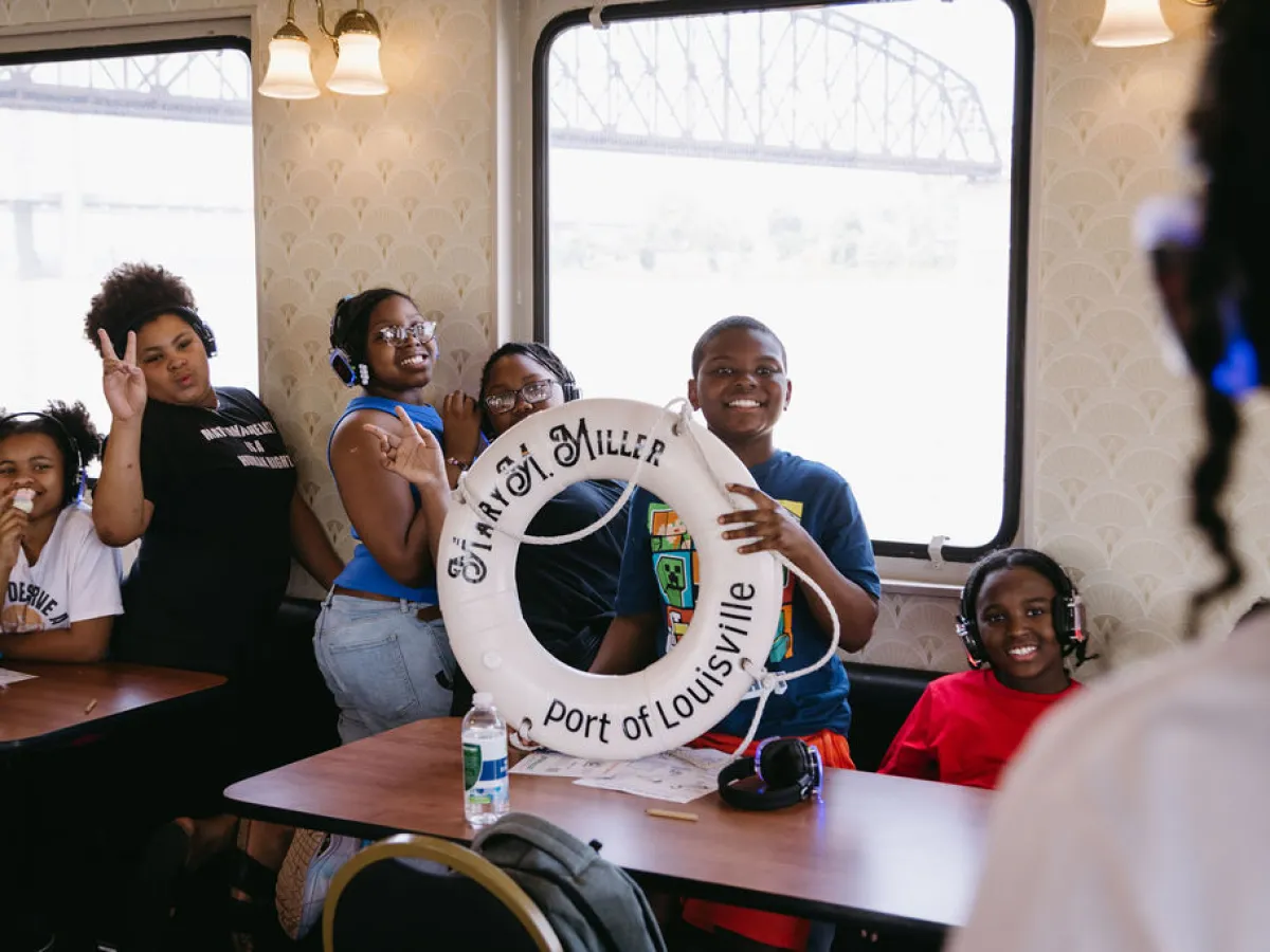 Group of kids on a boat posing with a life preserver labeled 'Port of Louisville.'