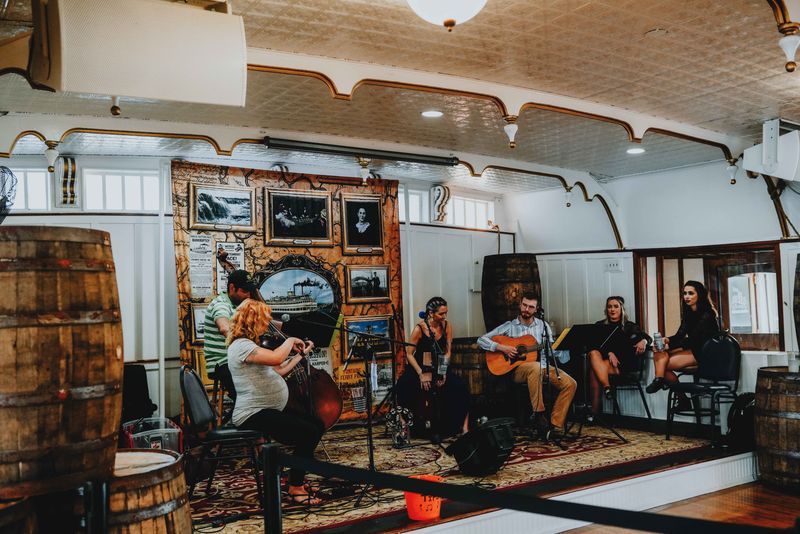 Musicians performing on a vintage-style stage with instruments and decorative barrels.