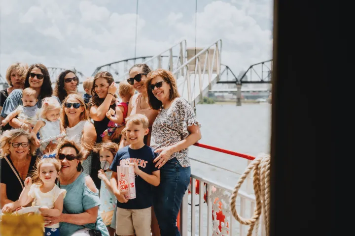 Group of people posing on a boat with a bridge in the background.