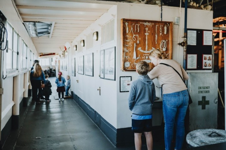 People exploring a ship's corridor with nautical displays on the walls.