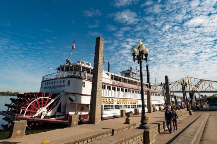 A paddleboat docked at a pier under a partly cloudy sky with people walking nearby.