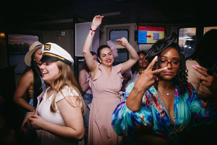 Group of people dancing and celebrating indoors, some wearing hats.