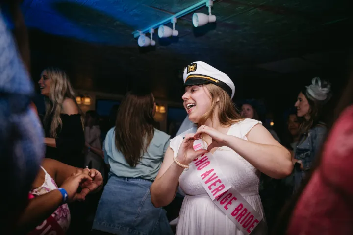 A woman in a captain's hat and sash dances at a party.