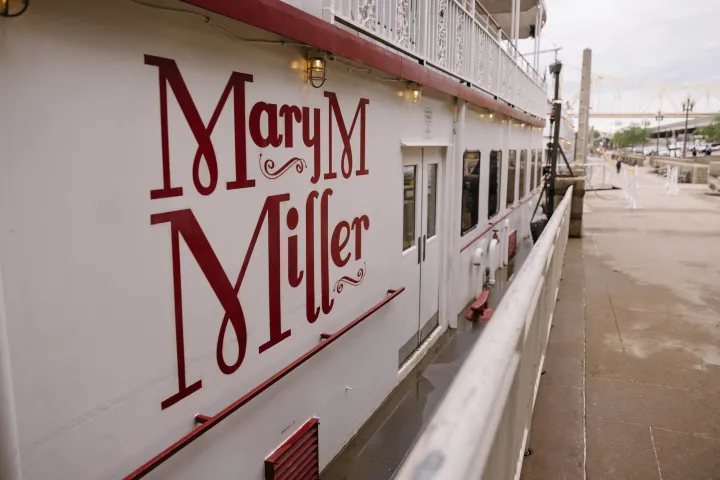 Docked riverboat with 'Mary M Miller' painted on its side, near a riverside walkway.